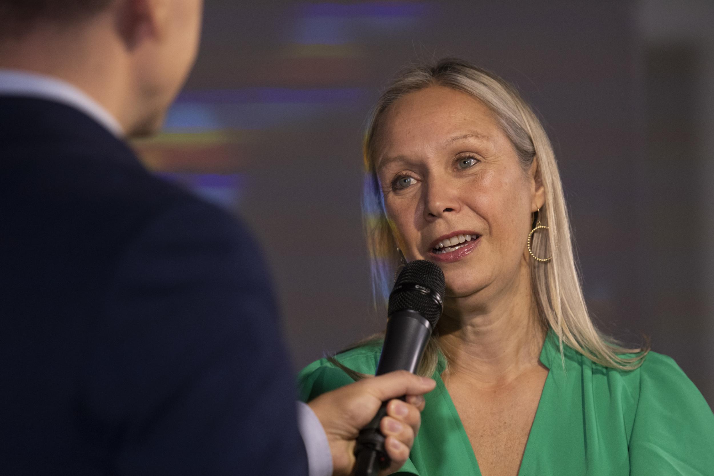 Lähikuva mikrofoniin puhuvasta naisesta vihreässä mekossa.